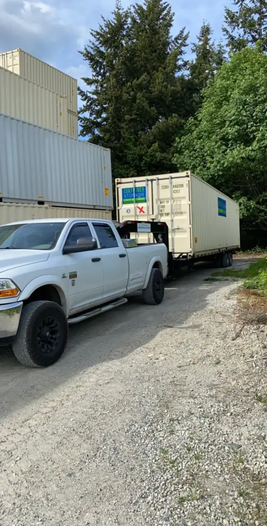 White pickup hauling a 40 foot shipping container on a tilt trailer
