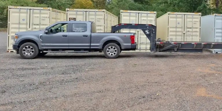 Pickup hitched to a gooseneck trailer in a yard of shipping containers