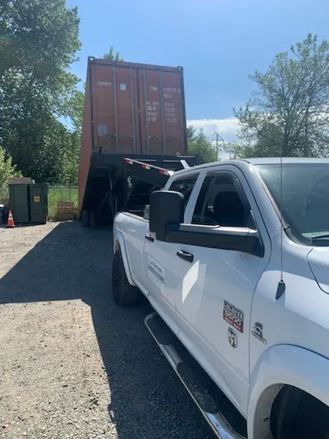 Shipping container raised on a tilt trailer behind a white work truck