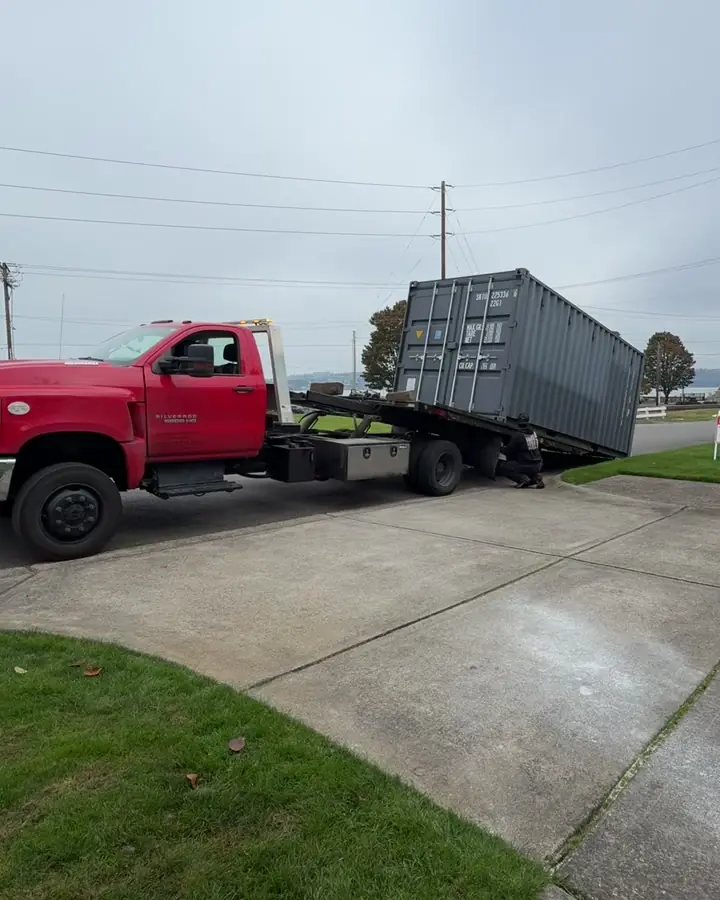 Shipping container being winched onto the tilted bed of a red truck