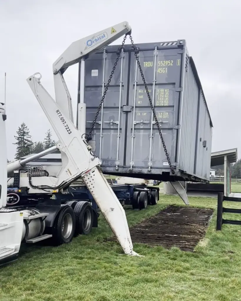 Side loader arm lowering a shipping container toward ground mats