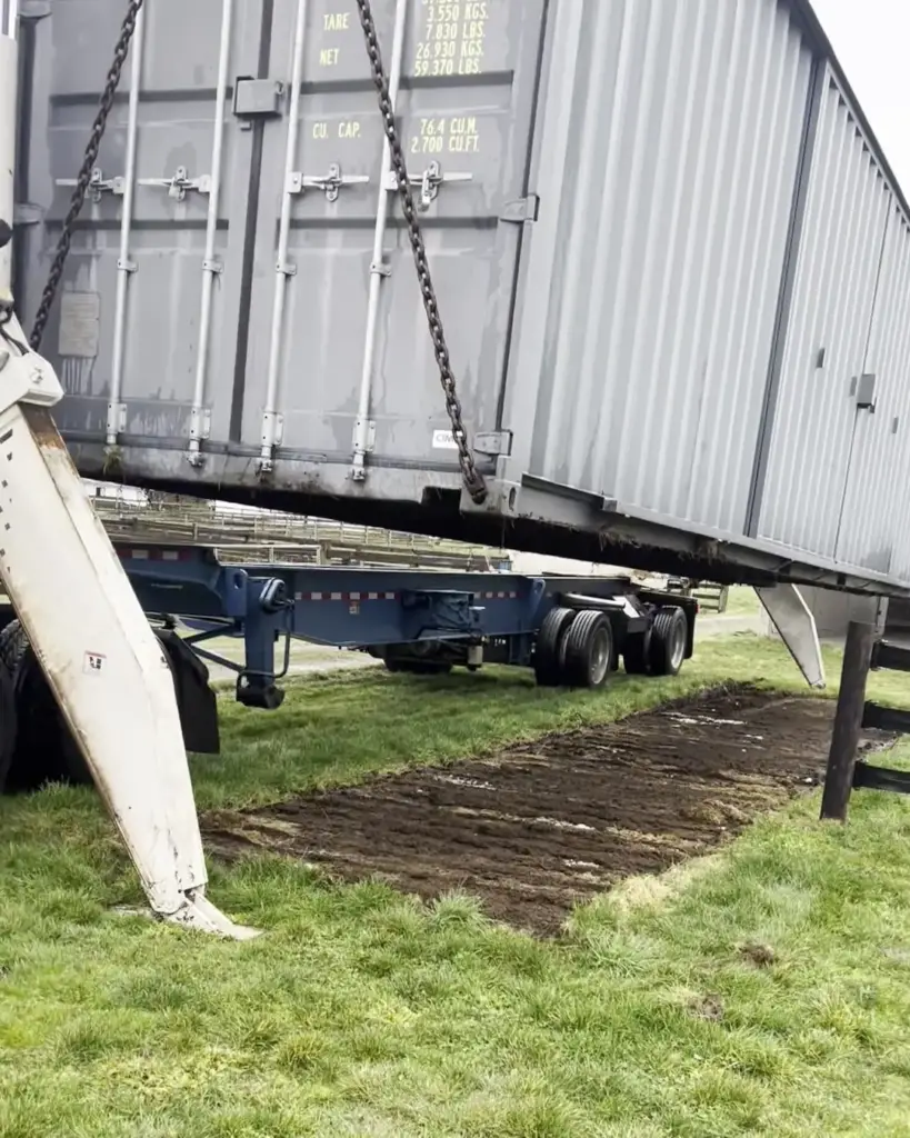 Side loader chains hooked to the bottom corners of a shipping container above ground mats